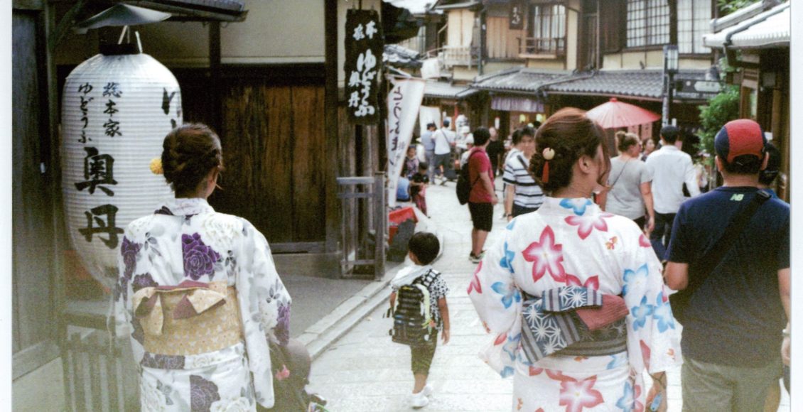 Two Japanese women in traditional clothing walk their children down a Kyoto street