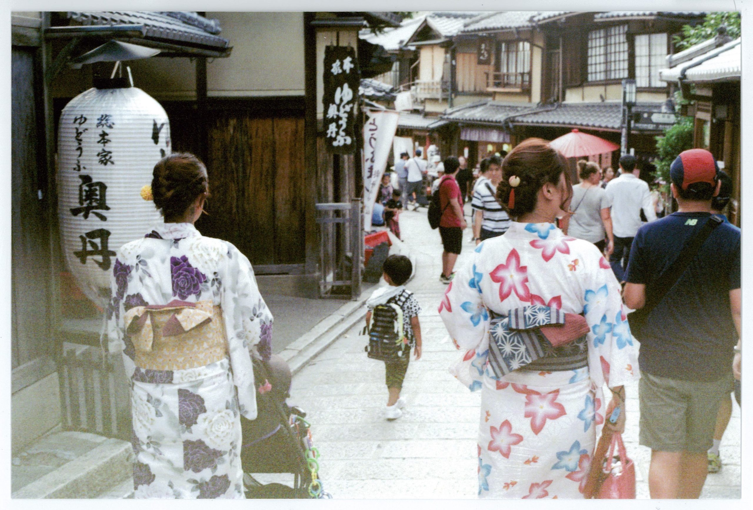 Two Japanese women in traditional clothing walk their children down a Kyoto street