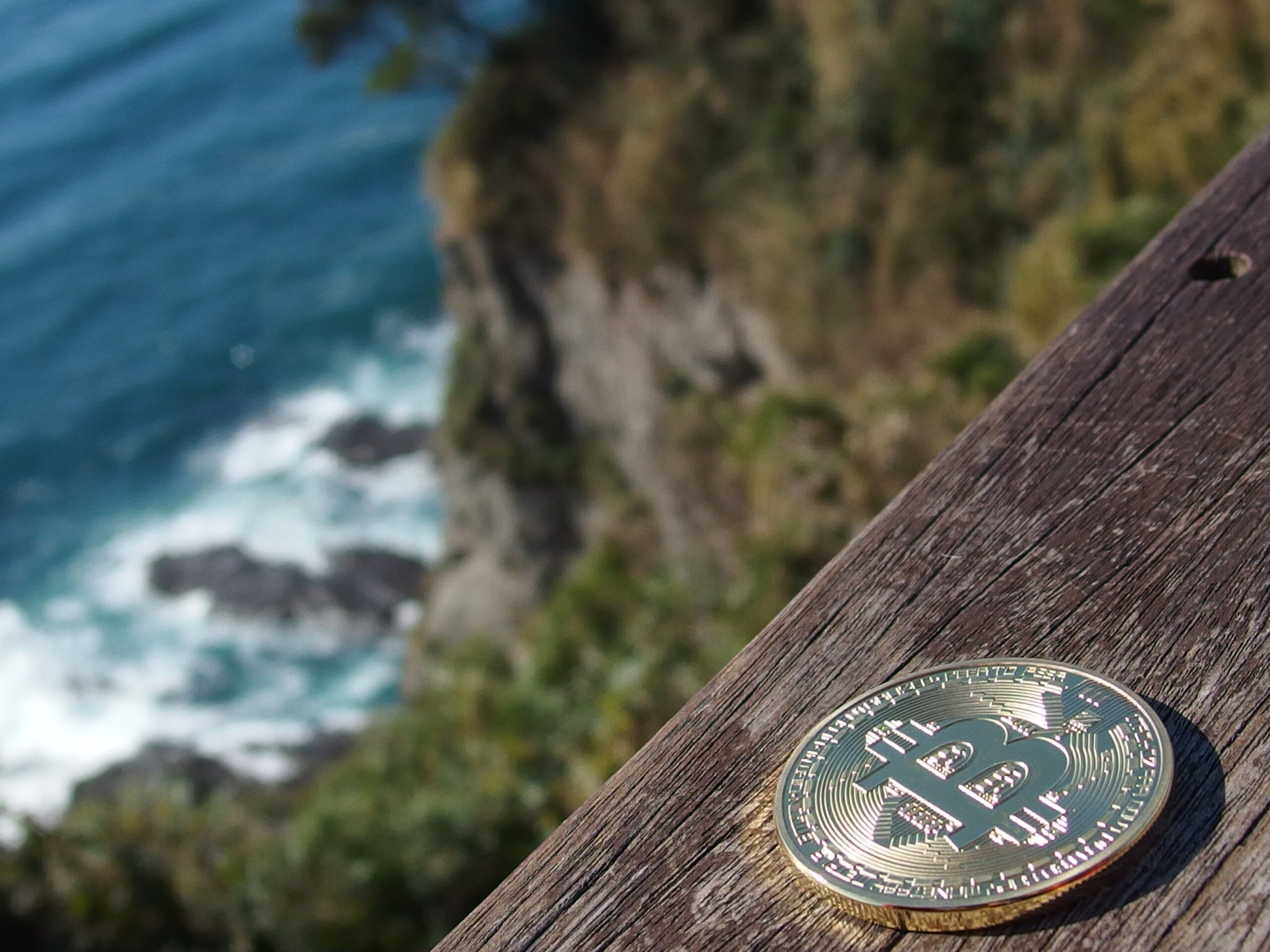 A Bitcoin Coin rests on a ledge overlooking a coastline